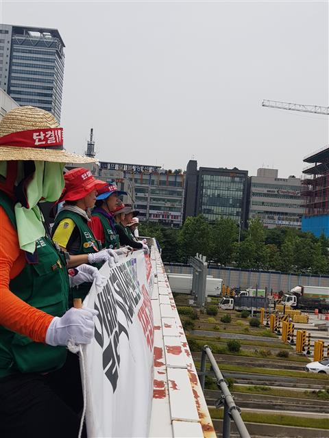 민주노총 민주일반연맹 톨게이트지부 소속 여성 노동자들이 지난 7월 4일 서울 톨게이트 구조물 위에서 ‘일방적 자회사 전환 중단하고 직접 고용하라’라고 쓰인 현수막을 들고 고공농성을 벌이고 있다.