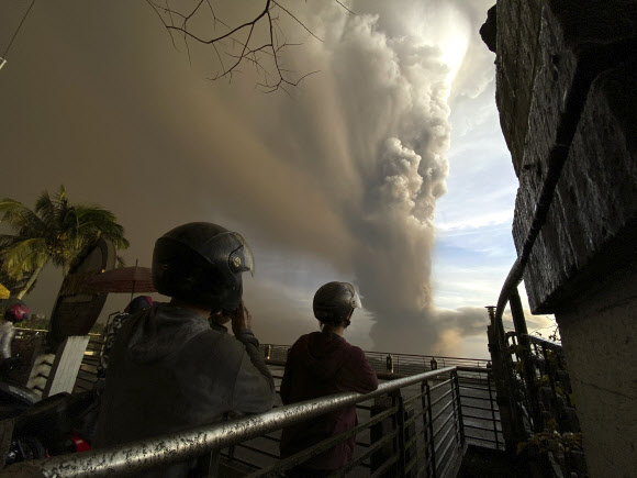 필리핀 수도 마닐라에서 남쪽으로 약 65㎞ 떨어진 탈 화산이 전날 폭발한 가운데, 타가이타이에서 오토바이 등으로 대피하기 위해 헬멧을 쓴 주민들이 화산재 기둥을 멍하니 바라보고 있다. 타가이타이 AP 연합뉴스