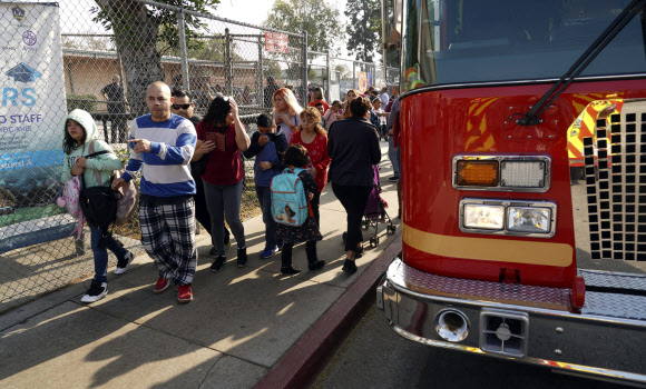 14일(현지시간) 항공유가 비처럼 내린 미국 로스엔젤레스 파크애비뉴 초등학교에서 한 학생이 소방차 옆을 지나고 있다. AP
