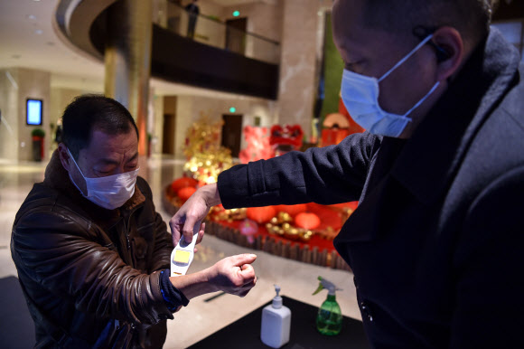 24일(현지시간) 중국 후베이성 우한시의 한 호텔에서 직원이 손님들의 체온을 측정하고 있다. AFP 연합뉴스