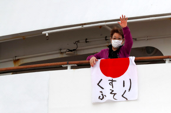 7일(현지시간) 일본 요코하마 다이코쿠 피어 크루즈 터미널에 정박해 있는 대형 크루즈선 다이아몬드 프린세스호에 승선한 한 여성이 ‘의약품 부족’이라고 적힌 일장기를 내걸고 있다. 로이터 연합뉴스