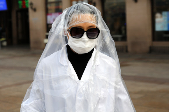 한 여성이 11일(현지시간) 중국 베이징 기차역에서 코로나바이러스로부터 보호하기 위해 마스크를 쓰고 머리까지 비닐가운을 덮고 이동하고 있다. EPA 연합뉴스