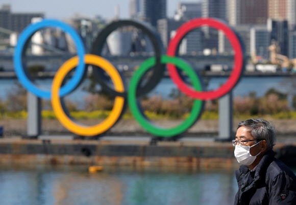 6일 일본 도쿄의 오다이바 해양공원에 세워진 올림픽 오륜 조형물 인근을 코로나19 예방 마스크를 쓴 시민이 지나가고 있다. 2020.3.10  로이터 연합뉴스