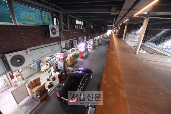 원래 차량 전용도로로 계획했던 1층에 비좁은 상점, 인도, 적치장, 1차선 차로와 주차장이 들어서 있다. 오른쪽에 다시세운 프로젝트의 일환으로 가설한 보행 데크가 2층에 떠 있다.   정연호 기자 tpgod@seoul.co.kr