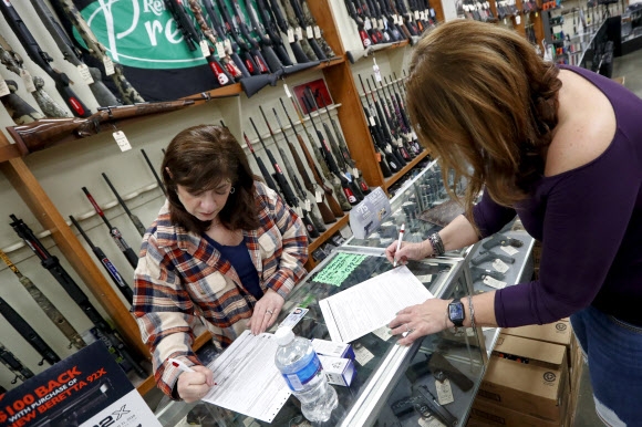 25일(현지시간) 미국 펜실베이니아주 뉴캐슬에 있는 한 총포상에서 총기를 사려는 한 여성(오른쪽)이 서류를 작성하고 있다. 총포상은 약국이나 편의점 같은 필수적인 영업장이 아니어서 매장 폐쇄 명령을 받았다. 뉴캐슬 AP 연합뉴스