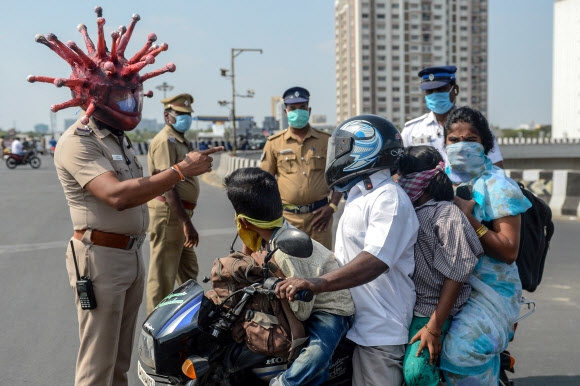 신종 코로나바이러스 감염증(코로나19) 확산에 대한 우려가 전세계적으로 커지고 있는 가운데 28일(현지시간) 인도 첸나이에서 코로나바이러스를 형상화한 헬멧을 쓴 경찰관이 시민들을 상대로 조사를 펼치고 있다. AFP 연합뉴스