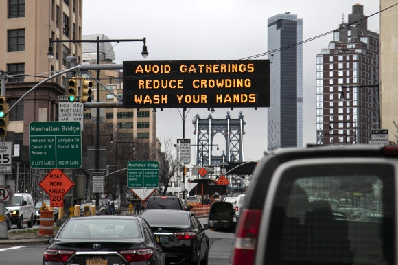 지난 19일(현지시간) 미국 뉴욕 맨해튼으로 들어가는 다리 앞에 모임을 줄이고 손을 씻으라는 내용의 경고문이 전광판에 표출되고 있다. AP통신