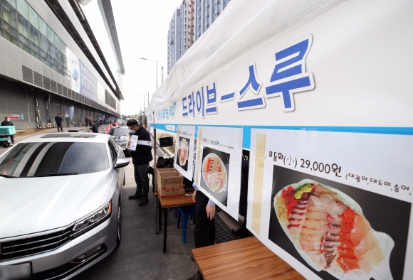  지난달 26일 서울 노량진수산시장 남1문 앞에서 시민들이 차에 탄 채 수산물을 사고 있다. 수협중앙회는 코로나19로 위축된 수산물 소비 활성화를 위해 차에 탄 채 물건을 구입할 수 있는 ‘드라이브 스루’(Drive through) 판매 방식을 도입했다. 박윤슬 기자 seul@seoul.co.kr   