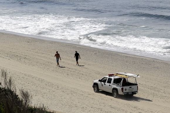 미국 캘리포니아주 도로순찰대가 지난달 25일 사회적(물리적) 거리 두기의 일환으로 칼스바드 해변을 봉쇄하며 서핑을 즐기던 남녀에게 빨리 떠날 것을 종용하고 있다. AP 자료사진 연합뉴스 