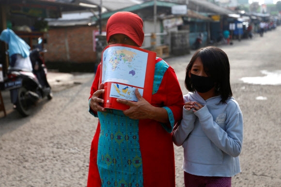 인도네시아 수도 자카르타 인근의 데폭에서 13일 마스크를 확보하지 못한 한 여성이 코로나19 전염을 우려해 책으로 입과 코를 가리고 걸어가고 있다. 2020-04-13 자카르타 로이터 연합뉴스