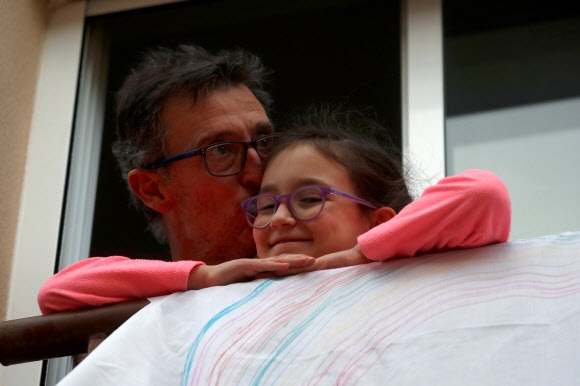 스페인 남부 론다에 사는 한 아빠가 18일(현지시간) 창문을 열어 의료진을 응원하는 무지개 그림을 펼친 채 격려의 박수를 함께 보낸 딸의 이마에 입을 맞추고 있다. 론다 로이터 연합뉴스 