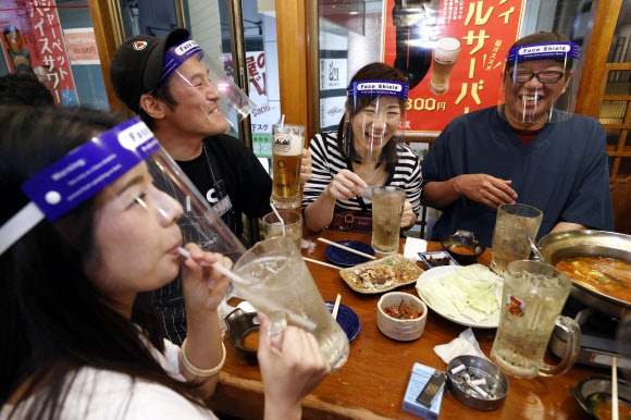 지난 25일 일본 오사카의 한 식당에서 페이스 쉴드를 착용한 일본인들이 둘러앉아 식사를 하며 일상을 즐기고 있다.  AP 연합뉴스