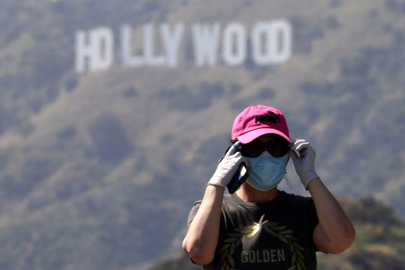 마스크를 하고 장갑을 낀 시민이 로스앤젤레스 할리우드 간판이 보이는 산책길에서 전화를 받고 있다. 그리피스 공원의 산책길은 지난주 일부 개방됐다. 연합뉴스  