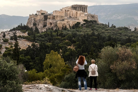 그리스 아테네의 프닉스 언덕을 찾은 여성들이 29일(현지시간) 이 도시를 대표하는 고대 유적 아크로폴리스를 올려다 보고 있다. 이날 그리스 정부는 코로나19 감염병을 극복한 29개국 관광객들을 다음달 중순부터 받아들이는 봉쇄 완화책을 발표했다. 아테네 AFP 연합뉴스 