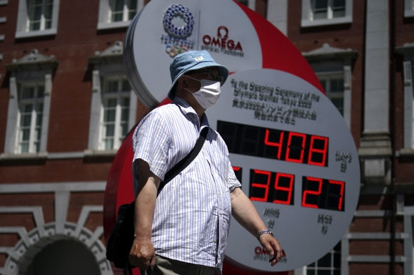 10일 일본 도쿄에 있는 내년 도쿄올림픽 개막일까지의 시간을 가리키는 시계 앞을 한 시민이 마스크를 쓰고 지나가고 있다. 2020.6.10  AP 연합뉴스