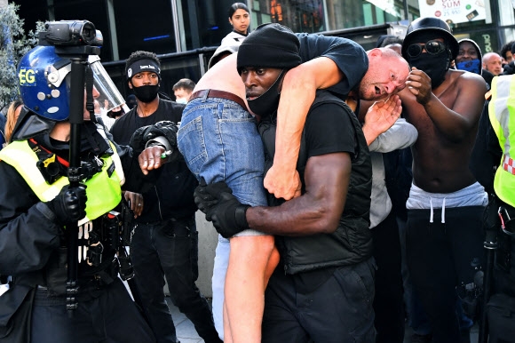 인종차별 반대 시위가 벌어진 13일(현지시간) 영국 런던에서 흑인 남성 패트릭 허친슨이 시위대와 극우 과격주의자들의 충돌 과정에서 다친 극우 시위대 쪽 백인 남성을 둘러메고 안전한 곳으로 옮기고 있다. 런던 로이터 연합뉴스