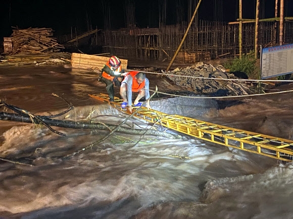 구조대원이 3일(현지시간) 중국 장시성 진안군 공사장에서 홍수로 고립된 근로자의 사다리 건너는 것을 돕고 있다. AP 연합뉴스