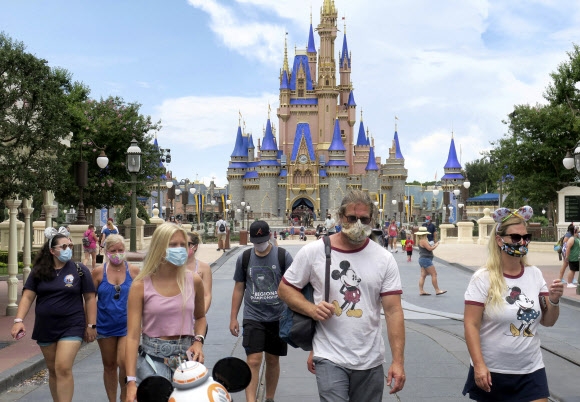 미국 플로리다주 올랜도의 디즈니월드가 재개장한 11일(현지시간) 방문객들이 마스크를 쓴 채로 이동하고 있다. AP 연합뉴스