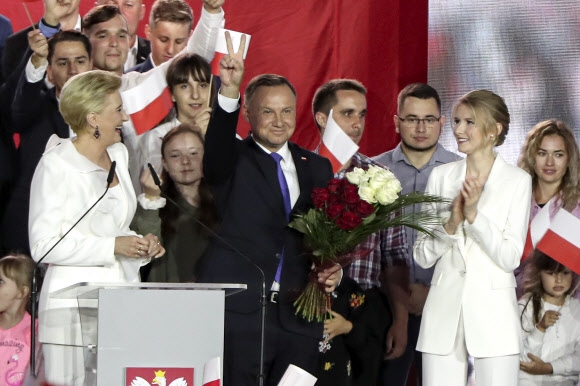 안제이 두다 폴란드 현 대통령(가운데)이 12일(현지시간) 지방도시 푸워투스크에서 열린 군중 집회에서 부인(왼쪽)과 딸(오른쪽)이 지켜보는 가운데 손가락으로 ‘V’자를 그리고 있다. 두다 대통령은 이날 대선 결선투표 종료 후 발표된 출구조사에서 50.4%를 득표할 것으로 예측돼 오차범위 내에서 경쟁자를 약간 앞섰다. 푸워투스크 AP연합뉴스