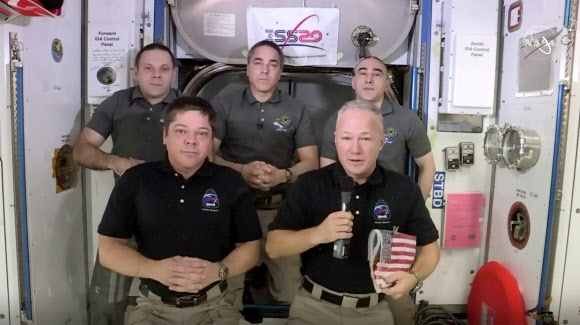 2일 오후(현지시간) 지구에 귀환하기 위해 국제우주정거장(ISS)과 분리될 예정인 유인 캡슐 크루 드래건으로 향하는 ISS의 해치 앞에서 더그 헐리(앞줄 오른쪽)가 1일 밥 벤켄(앞줄 왼쪽)과 크리스 캐시디(뒷줄 가운데) 선장, 두 러시아인 우주인이 지켜보는 가운데 고별 기자회견 도중 소감을 밝히고 있다. 헐리가 들고 있는 성조기는 9년 전 버락 오바마 대통령이 선물한 것으로 우주왕복선이 퇴역한 뒤 줄곧 ISS에 있어 왔는데 이번에 두 우주인이 들고 귀환한다. NASA 제공 AP 연합뉴스