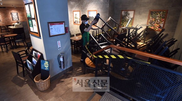 17일 오후 서울 중구의 한 스타벅스 매장에서 점원이 코로나19 확산 방지를 위해 좌석을 30% 축소하며 한쪽 구석에 빼놓은 의자와 테이블을 정리하고 있다.  정연호 기자 tpgod@seoul.co.kr
