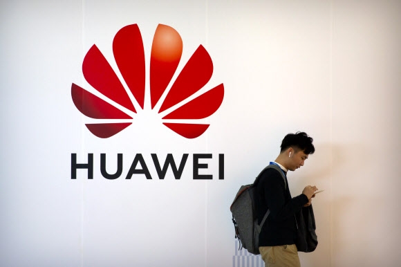 미국이 중국 최대 통신장비 업체인 화웨이 고사작전에 나선 가운데 지난해 10월 베이징 화웨이 로고 광고판 앞을 한 남성이 스마트폰을 보면서 지나가고 있다.  베이징 AP 연합뉴스