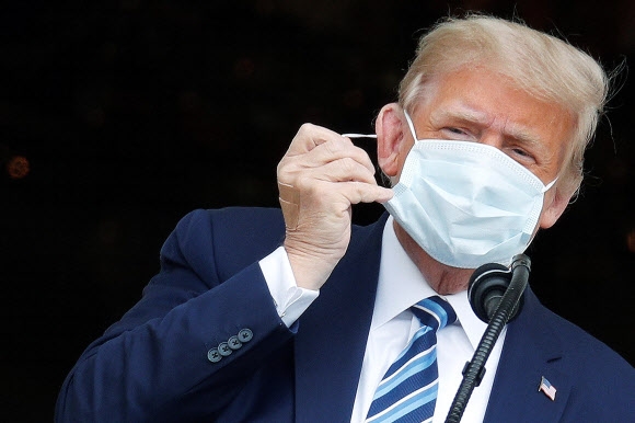 도널드 트럼프 미국 대통령이 연설을 하기 위해 마스크를 벗으려 하고 있다. 2020.10.11 워싱턴 로이터 연합뉴스