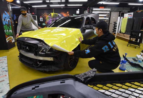 경기 군포의 자동차 튜닝업체 카스킨코리아에서 작업자들이 차량에 노란색 래핑 필름을 입히는 작업을 하고 있다.