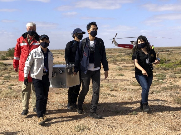 일본 우주항공연구개발기구(JAXA) 요원들이 6일 호주 사우스 오스트레일리아주 우메라 사막지대에 떨어진 소행성 류구의 내부물질을 담은 캡슐을 회수해 호주항공우주국(ASA) 지원시설 안으로 옮기고 있다. ASA 제공 AP 연합뉴스  