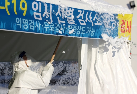 31일 광주광역시 시청광장에 마련된 코로나19 임시 선별검사소에서 의료진이 천막에 쌓인 눈을 제거하고 있다. 연합뉴스