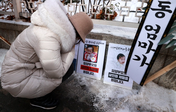 16개월 된 입양 딸 정인 양을 학대해 숨지게 한 혐의를 받는 양부모의 첫 재판이 열린 13일 서울 양천구 남부지방법원에서 재판이 끝난 뒤 한 시민이 법원 청사 앞에 놓인 정인 양의 사진이 담긴 패널 앞에서 정인 양을 추모하고 있다. 2021.1.13 연합뉴스