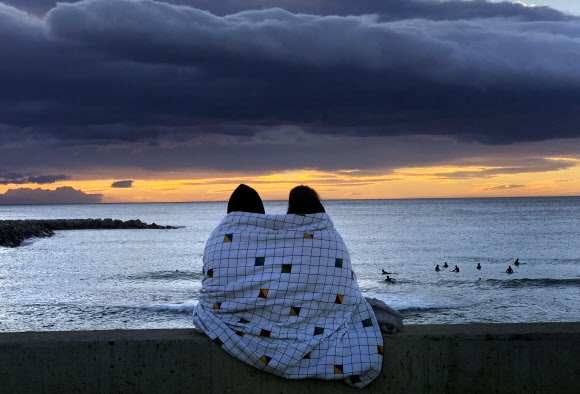 한 커플이 24일(현지시간) 스페인 바르셀로나 지중해 앞에서 일출을 보면서 담요를 함께 덮고 있다. AP 연합뉴스