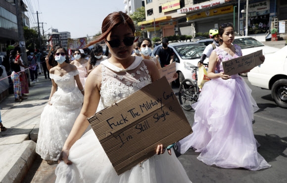 무도복과 결혼 드레스를 입은 미얀마 여성들이 10일 양곤 길거리에 나와 군부 쿠데타에 반대하는 격문을 들고 행진하고 있다. 격문에는 ‘군부 쿠데타 엿 드세요. 난 여전히 싱글’이라고 적혀 있다. 양곤 AP 연합뉴스 