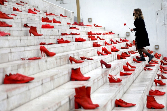 8일(현지시간) 알바니아 티라나에서 여성에 대한 폭력 중단을 의미하며 시내 광장에 전시된 빨간 신발들 옆으로 한 여성이 지나가며 붉은 꽃을 놓고 있다. 티라나 AFP 연합뉴스