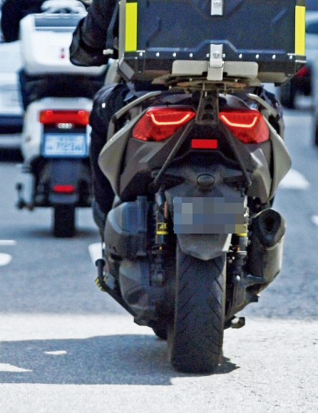 도로를 주행 중인 한 배달 오토바이의 번호판이 이물질로 까맣게 덮여 있어 식별하기 어렵다.