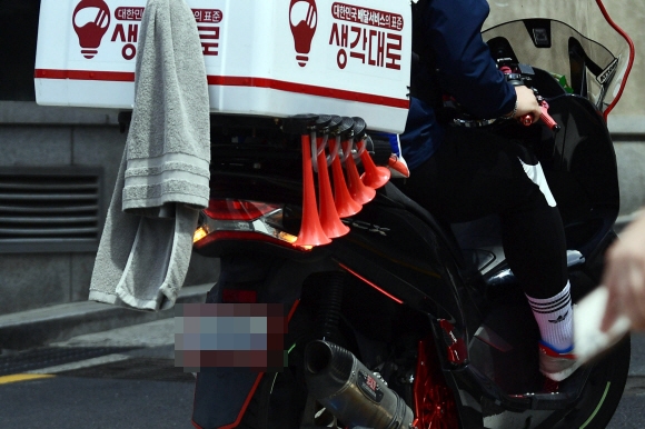 한 배달 오토바이가 후면과 측면에 수건과 액세서리 등을 부착해 번호판을 가리며 주행하고 있다.