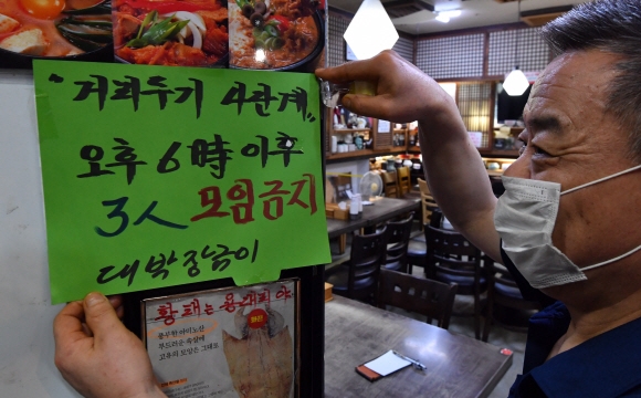 12일 서울 종로구의 한 식당에서 식당주인이 오후6시 이후 3인이상 집합금지를 알리는 게시글을 붙이고 있다. 2021.7.12 박지환기자 popocar@seoul.co.kr