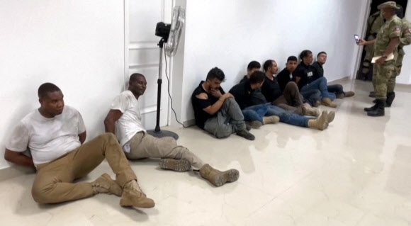 조브넬 모이즈 아이티 대통령이 지난 7일(이하 현지시간) 암살된 다음날 아이티 경찰이 체포해 취재진에 공개했을 때 촬영된 동영상을 캡처한 사진 중 하나. 흰색 상의를 걸친 두 사람이 콜롬비아 용의자들과 확연하게 체구와 외모도 구분돼 아이티계 미국인 용의자 조제프 뱅상(55)과 제임스 솔라주(35)일 것으로 추정된다. AFP 자료사진 연합뉴스 
