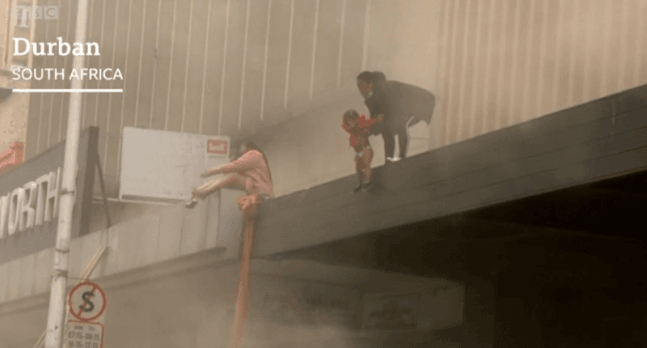 남아공 더반의 한 주상복합 건물. 1층 상점에 불이 나자 건물 윗층에 있던 아기 엄마가 아기를 사람들의 품에 던지고 있다. BBC 캡처.