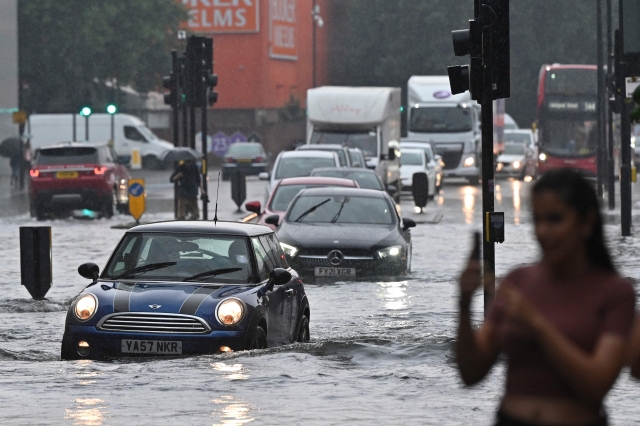 지난 25일(현지시간) 영국 런던에 내린 기록적인 폭우가 내린 가운데 차량들이 물에 잠긴 도로 위를 지나가고 있다. AFP 연합뉴스
