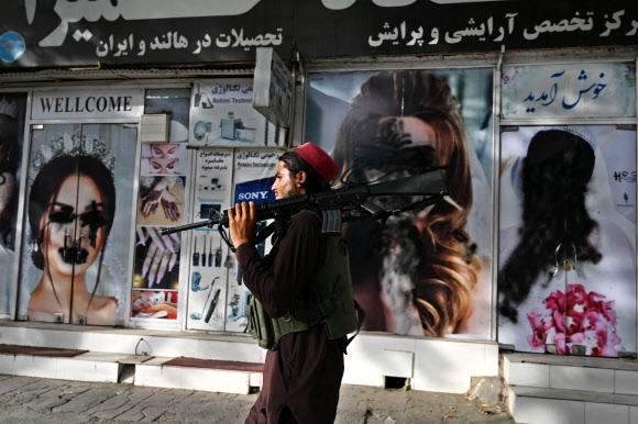 무장한 탈레반이 18일 아프간 수도 카불에서 훼손된 여성 포스터 앞을 지나고 있다. AFP 연합뉴스