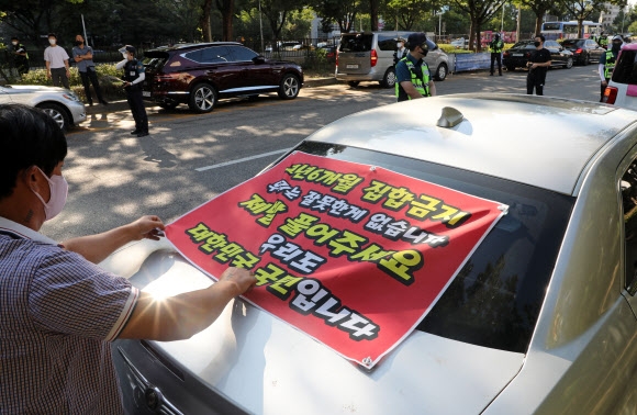 15일 서울 영등포구 국회 근처에서 한국유흥음식업중앙회 회원이 차량에 코로나19 집합금지 업종을 풀어 달라는 현수막을 붙이고 있다. 경찰은 이들의 차량 시위를 불법으로 간주하고 통행을 제한했다. 연합뉴스