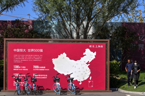 지난 9월 22일 중국 베이징의 헝다(恒大·에버그란데) 신규주택 개발부지에서 사람들이 헝다의 개발 프로젝트를 보여주는 안내판 옆을 지나고 있다. 베이징 AP 연합뉴스