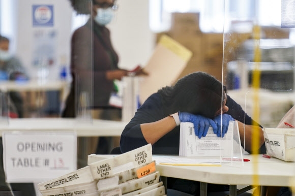 지난해 11월 10일 미국 대선의 부재자 투표 용지를 개표하던 뉴욕의 개표 직원이 잠시 엎드려 쉬고 있다. AP 연합뉴스