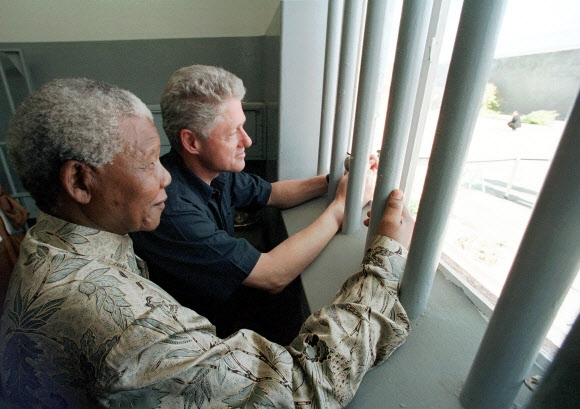지난 2013년 세상을 떠난 넬슨 만델라 남아공 대통령이 18년 동안 수감돼 있던 루벤섬 교도소의 감방을 1998년 3월 27일(현지시간) 빌 클린턴 전 미국 대통령과 함께 찾아 안에서 밖을 내다보며 감회에 젖고 있다. AP 자료사진 연합뉴스 