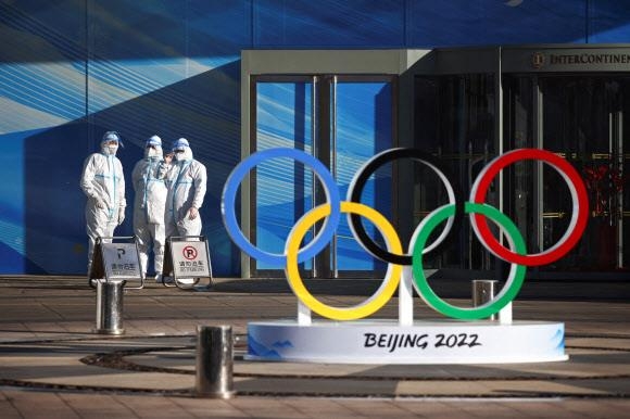 2022 베이징동계올림픽 개·폐막식이 열리는 베이징 국가경기장 인근 공사 현장에서 방역복을 입은 직원들이 오륜 상징물 옆에서 대기하고 있다.  베이징 로이터 연합뉴스