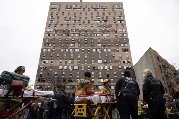   미국 뉴욕 경찰관들과 소방대원들이 9일(현지시간) 일어난 큰 불로 어린이 9명 등 19명이 숨진 브롱크스의 19층짜리 아파트 건물 아래에서 작업하고 있다. 수많은 인명 피해가 유독성 연기 때문에 일어나 정작 건물 외관은 일부 층에 그을린 자국이 있고 유리창이 깨져있지만 멀쩡해 보인다. 뉴욕 AP 연합뉴스 