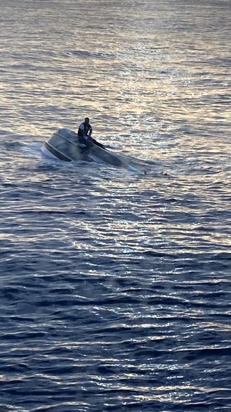 지난 25일(현지시간) 미국 플로리다주 동부 해안 근처에서 전복된 배의 밑바닥에 걸터 앉아 해안경비대에 의해 구조되기 직전의 남성 모습. 미국 해안경비대 제공 로이터 연합뉴스 