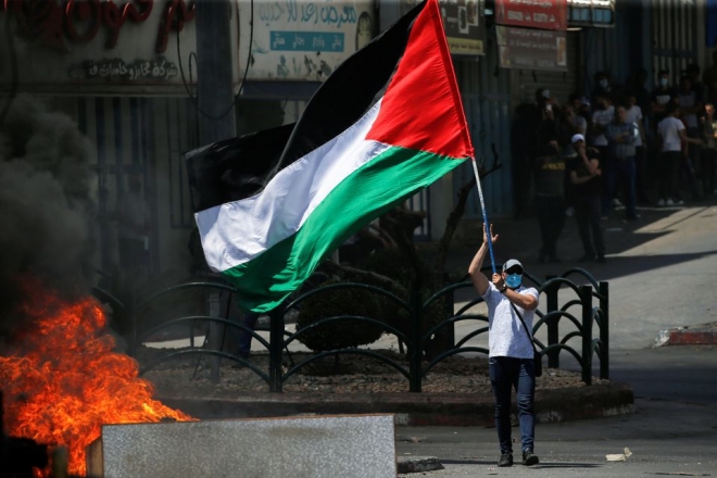 지난해 5월 18일 이스라엘이 점령한 요르단강 서안의 헤브론 도시에서 한 시위자가 이스라엘군의 가자지구 공습을 반대하는 반이스라엘 시위에 참여해 팔레스타인 국기를 들고 있다.  헤브론 로이터통신 연합뉴스