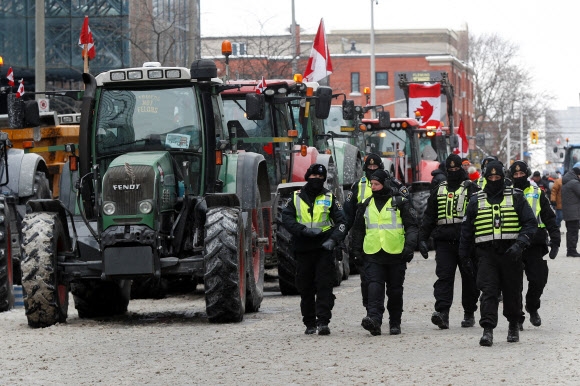 코로나19 백신 접종에 반대하는 트럭 운전사들의 시위로 무법지대가 된 캐나다 수도 오타와에서 6일(현지시간) 시 정부가 비상사태를 선포했다. 사진은 이날 경찰관들이 시위에 참여한 트랙터들 옆을 지나는 모습. 오타와 로이터 연합뉴스